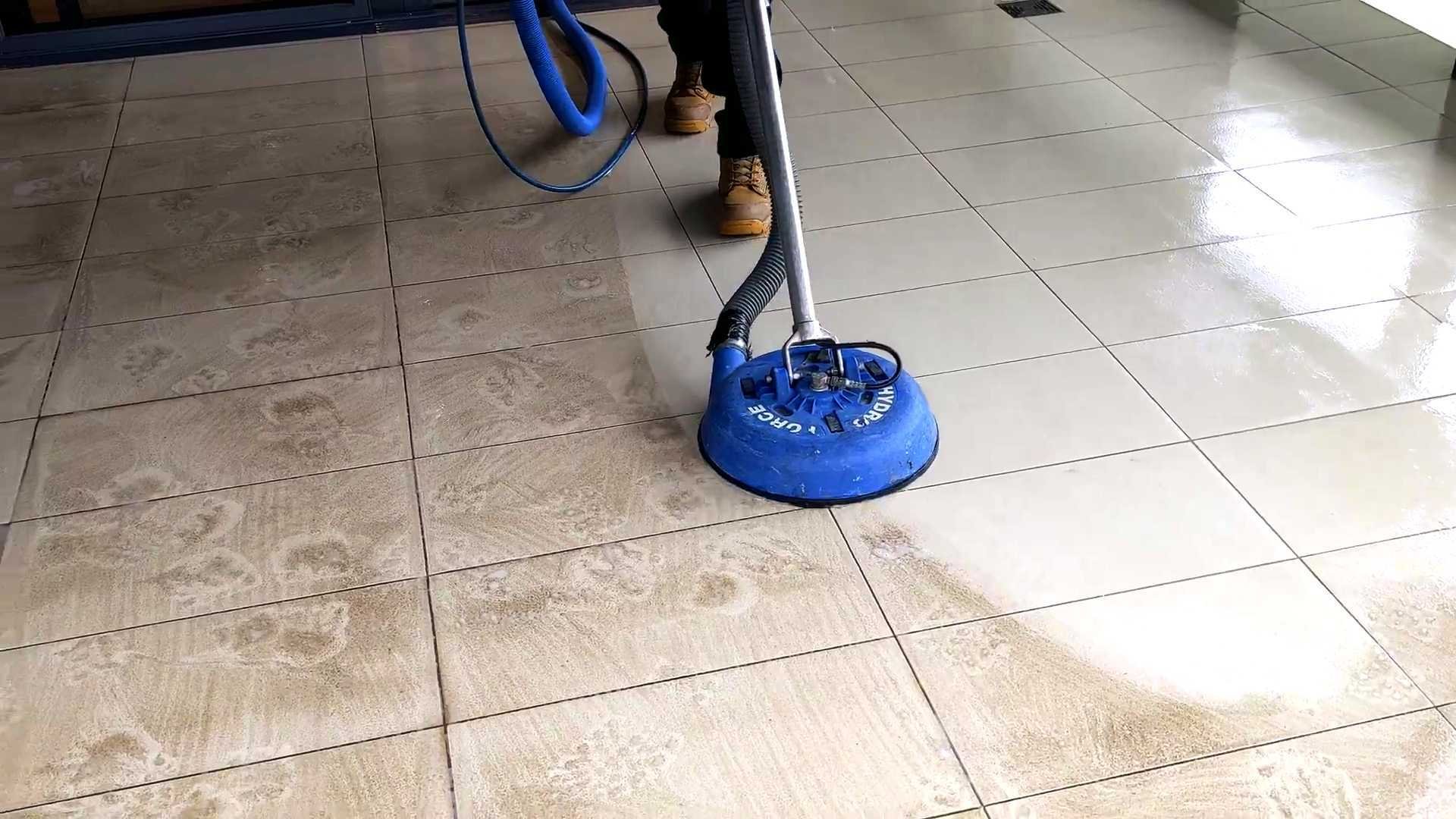 Blue surface cleaning machine on tiled floor with operator in background during cleaning service